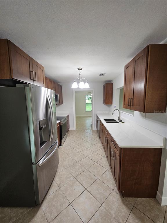 A galley kitchen features wood cabinets, white countertops, stainless steel appliances, and tiled flooring — 16225 BELLAMY BROTHERS BOULEVARD, DADE CITY, FL