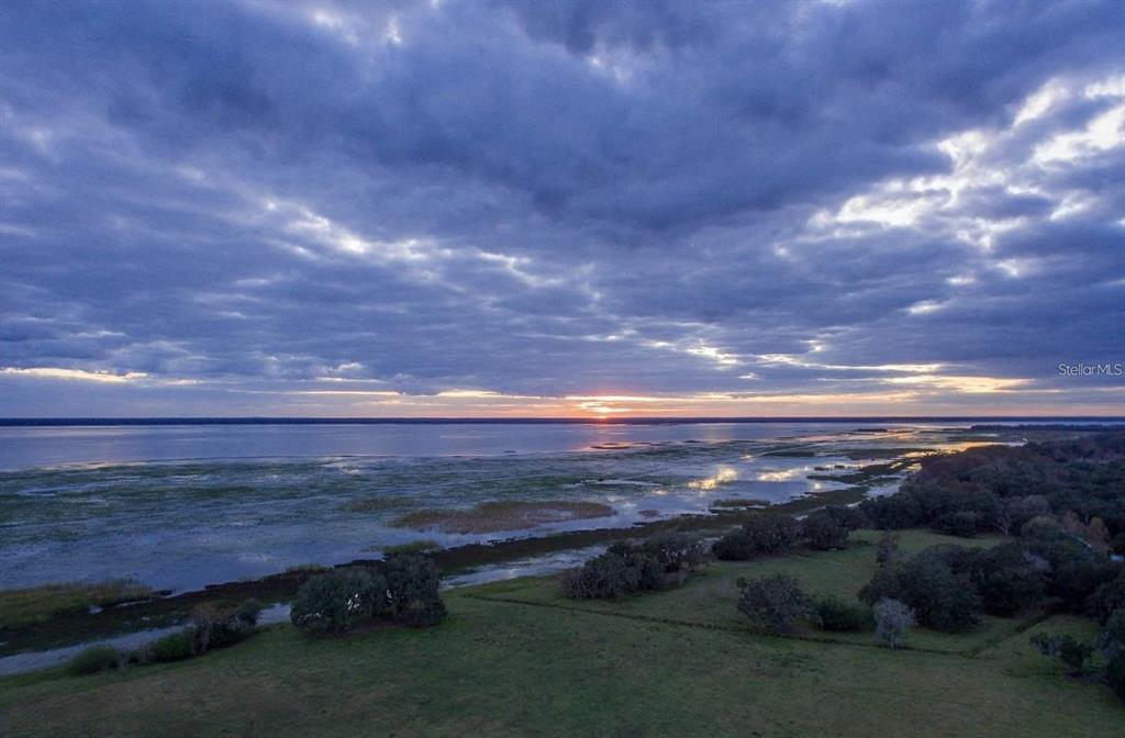 An aerial view of a grassy field bordering a large lake under a cloudy sunset — 3650 LAKE TOHOPEKALIGA ROAD, ST CLOUD, FL