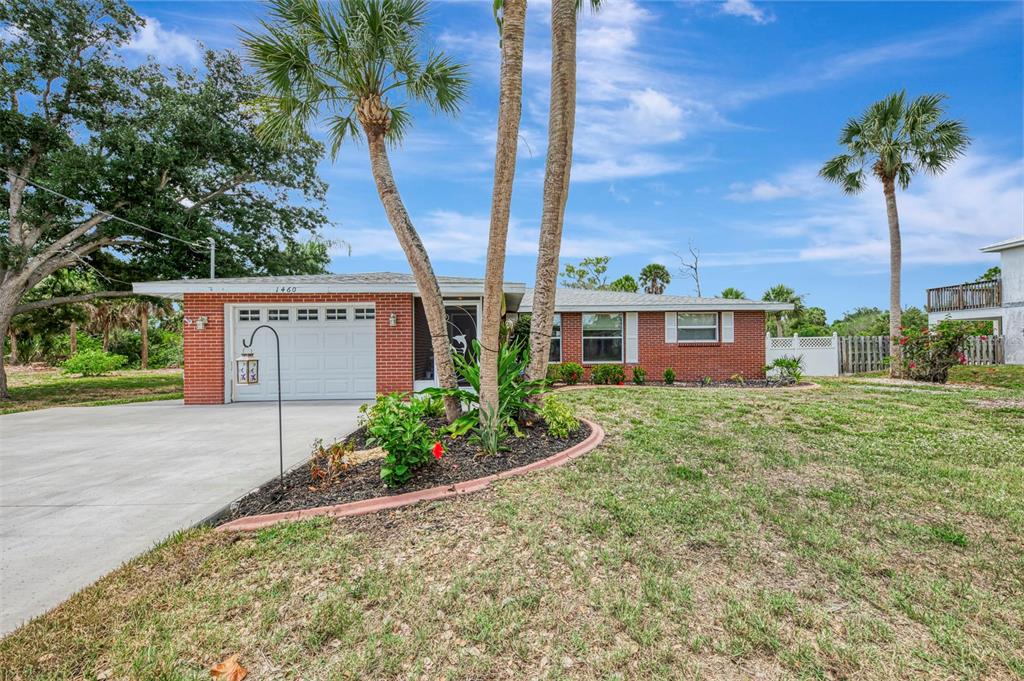 A single-story brick house with a concrete driveway, palm trees, and a front lawn — 1460 CORTES DRIVE, ENGLEWOOD, FL