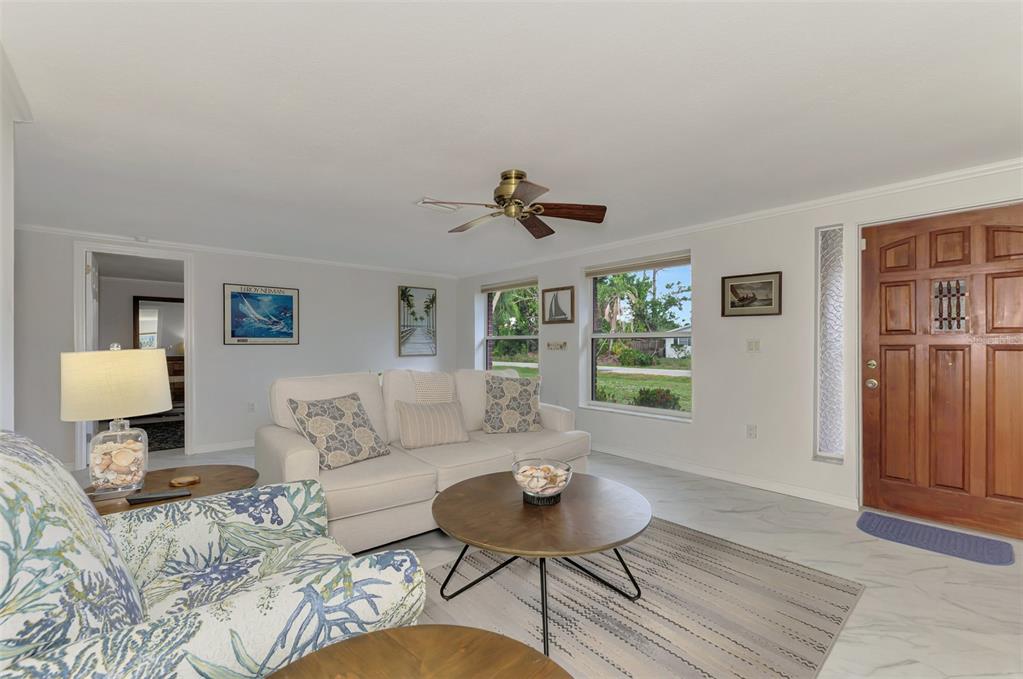 A living room features a white sofa, patterned armchair, round coffee table, and wood front door — 1460 CORTES DRIVE, ENGLEWOOD, FL