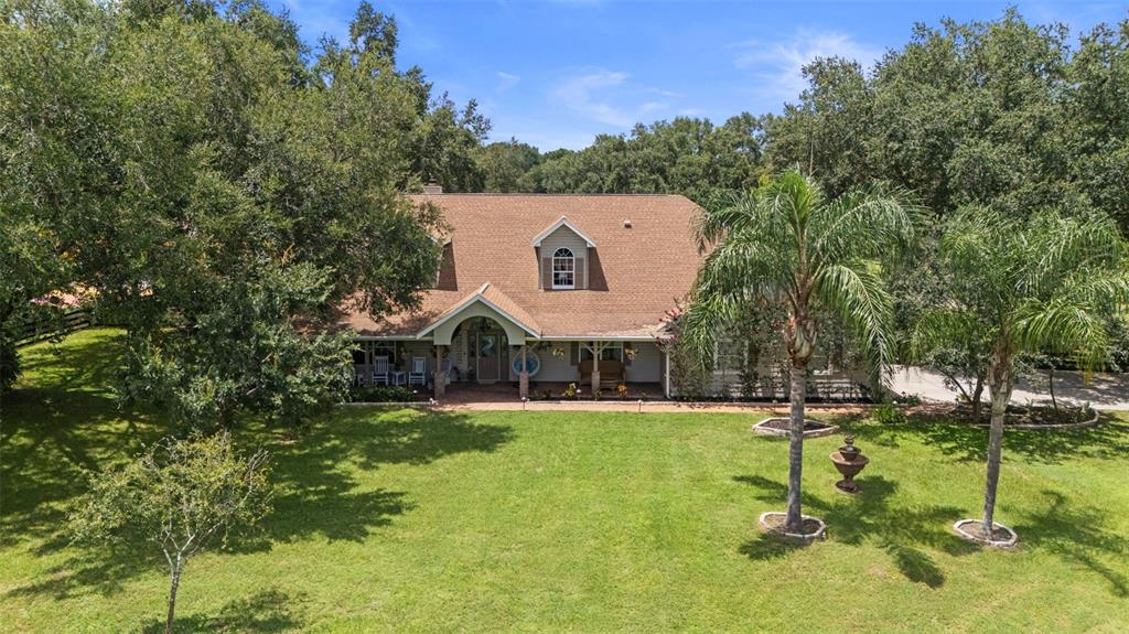 A covered brick porch features rocking chairs, a decorative bicycle planter, and vertical house numbers — 32137 WOLF BRANCH LANE, SORRENTO, FL