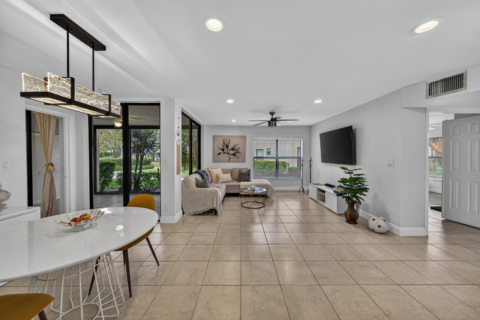 An open-concept living and dining area features tile flooring, a sectional sofa, and a chandelier — 8565 W Boca Glades Blvd # C, Boca Raton FL 33434, BOCA RATON, FL