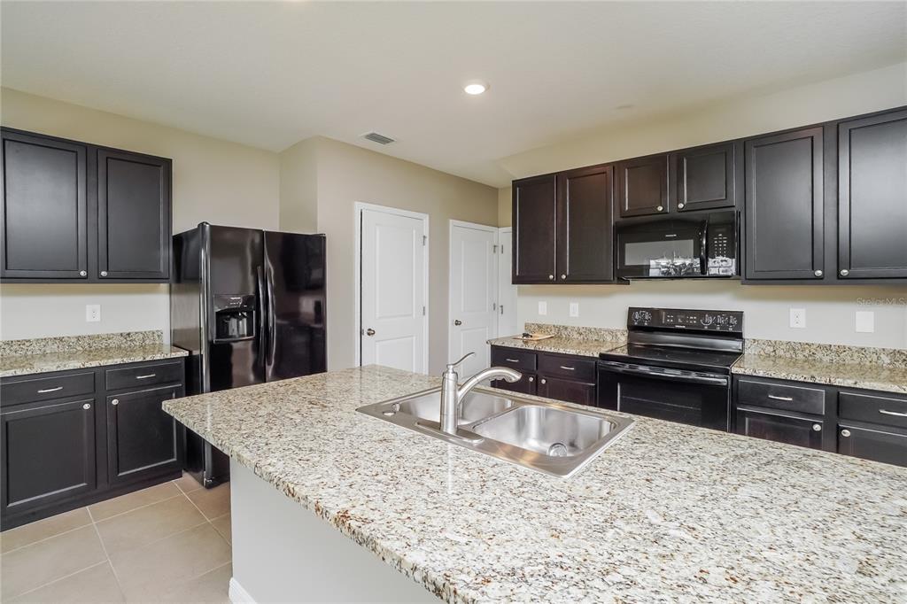 A kitchen features dark cabinetry, granite countertops, a central island with a sink, and appliances — 16726 SECRET MEADOW DRIVE, ODESSA, FL