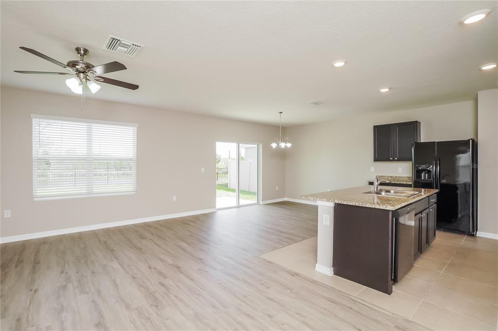 An open-concept living area features wood-look flooring, a kitchen island, and a sliding glass door — 16726 SECRET MEADOW DRIVE, ODESSA, FL