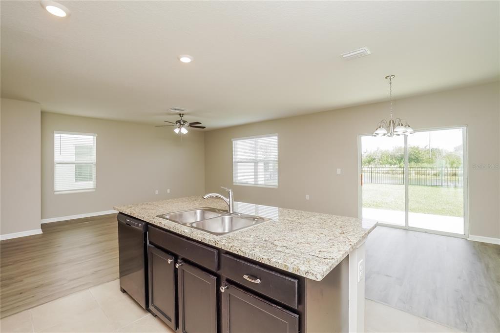 A kitchen island with a granite countertop and sink overlooks an open-concept living and dining area — 16726 SECRET MEADOW DRIVE, ODESSA, FL