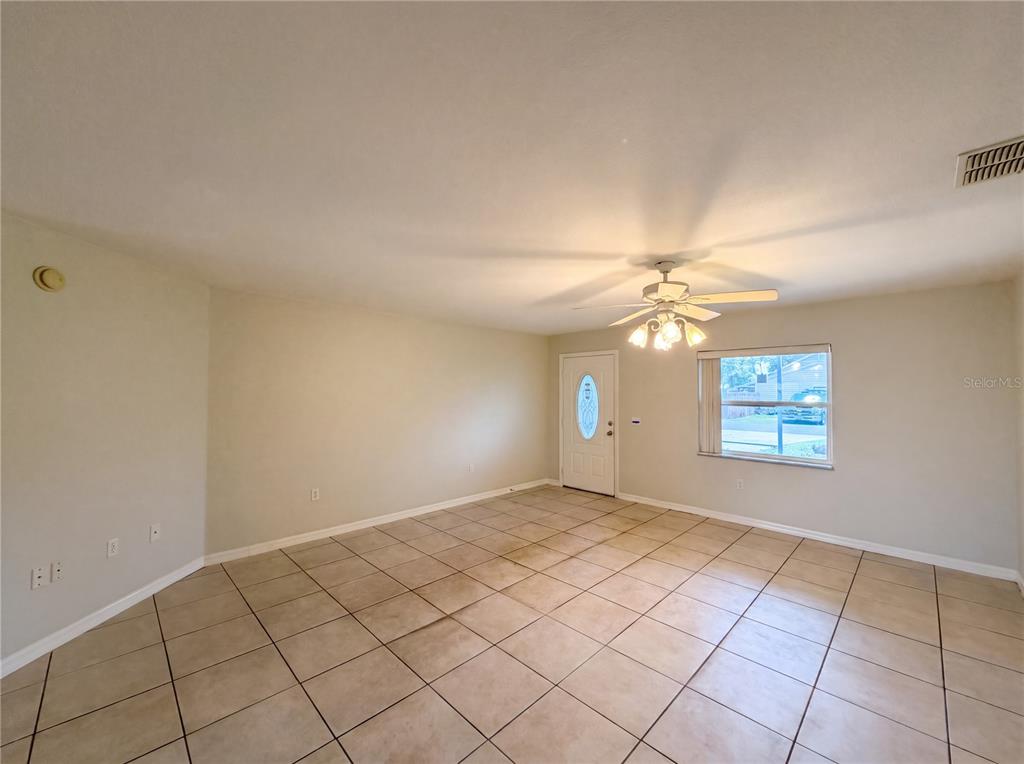 An empty room features beige tile flooring, light-colored walls, a ceiling fan, and a front door — 4846 MAC DONALD STREET, LAKE WALES, FL
