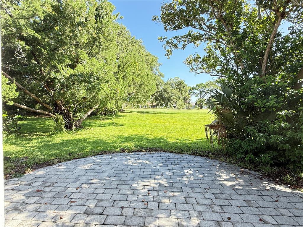 A circular paver patio overlooks a grassy backyard surrounded by mature trees — 33 ANDREA DRIVE, NEW SMYRNA BEACH, FL