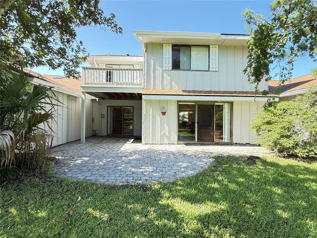 A two-story house exterior features a paved patio, a wooden balcony, and vertical siding — 33 ANDREA DRIVE, NEW SMYRNA BEACH, FL