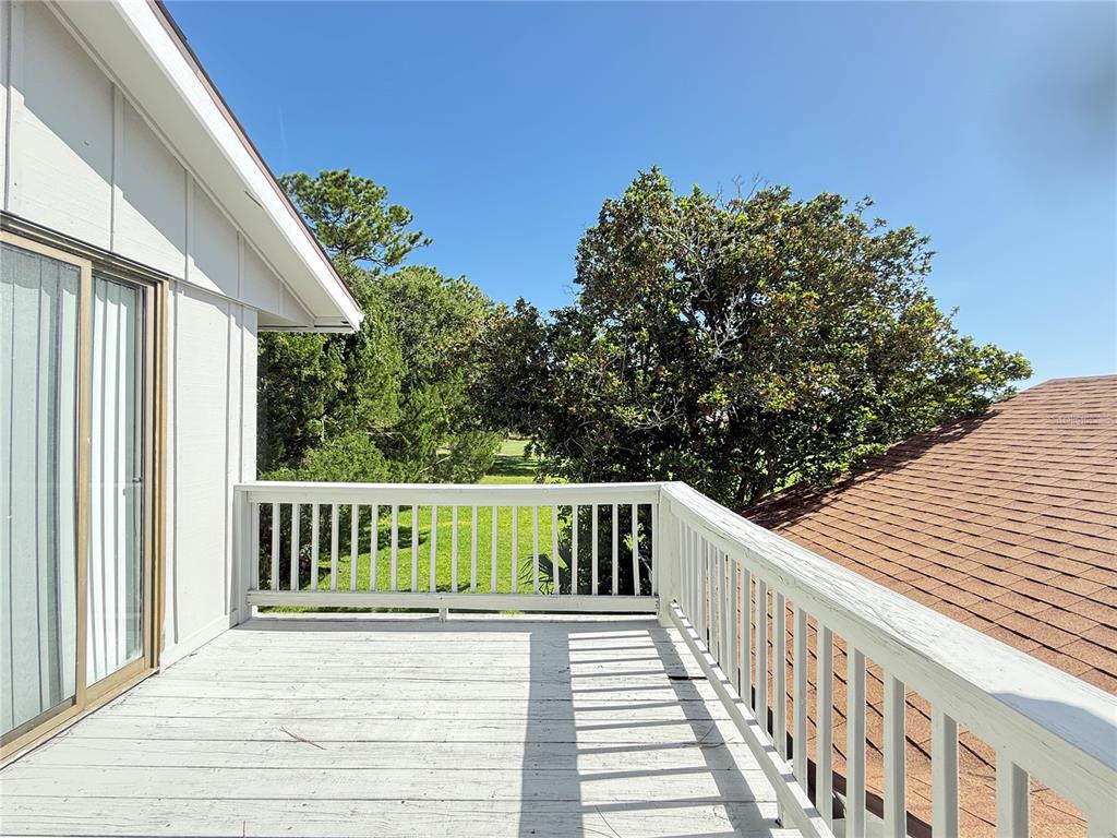 A wooden deck with white railings overlooks trees and a neighboring roof under a clear sky — 33 ANDREA DRIVE, NEW SMYRNA BEACH, FL