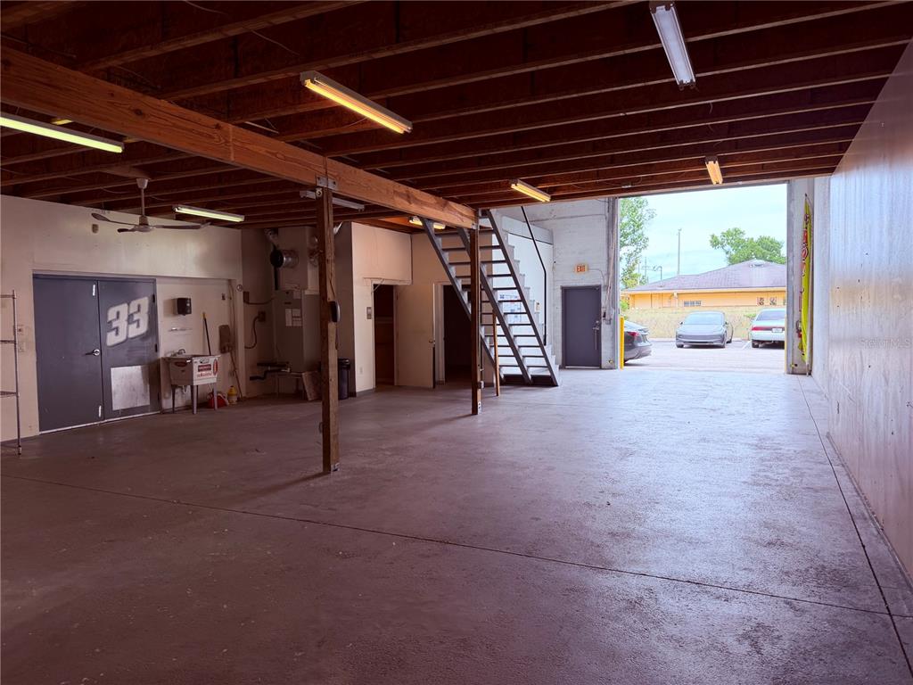 An open warehouse space features a concrete floor, exposed ceiling beams, and a metal staircase — 4415 N LOIS AVENUE, TAMPA, FL