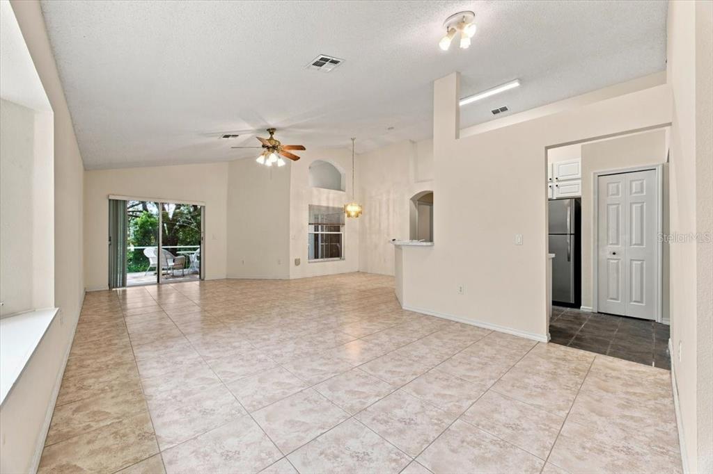 An open-concept living and dining area features beige tile flooring, a vaulted ceiling, and sliding doors — 2393 PAULETTE DRIVE, HAINES CITY, FL