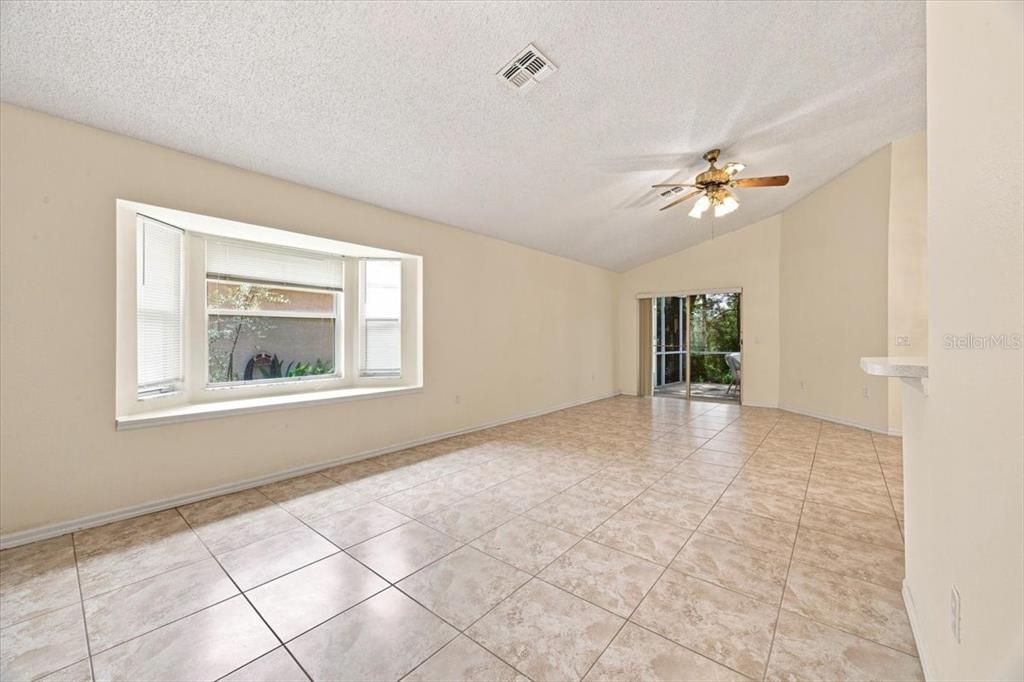 An empty living room features beige tile flooring, a bay window, and a vaulted ceiling — 2393 PAULETTE DRIVE, HAINES CITY, FL