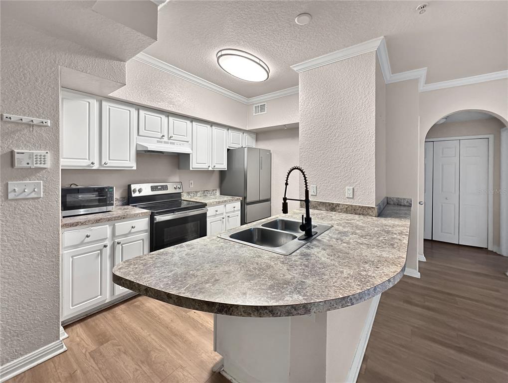 A kitchen features white cabinets, stainless steel appliances, a curved countertop, and a double sink — 911 N ORANGE AVENUE UNIT 232, ORLANDO, FL