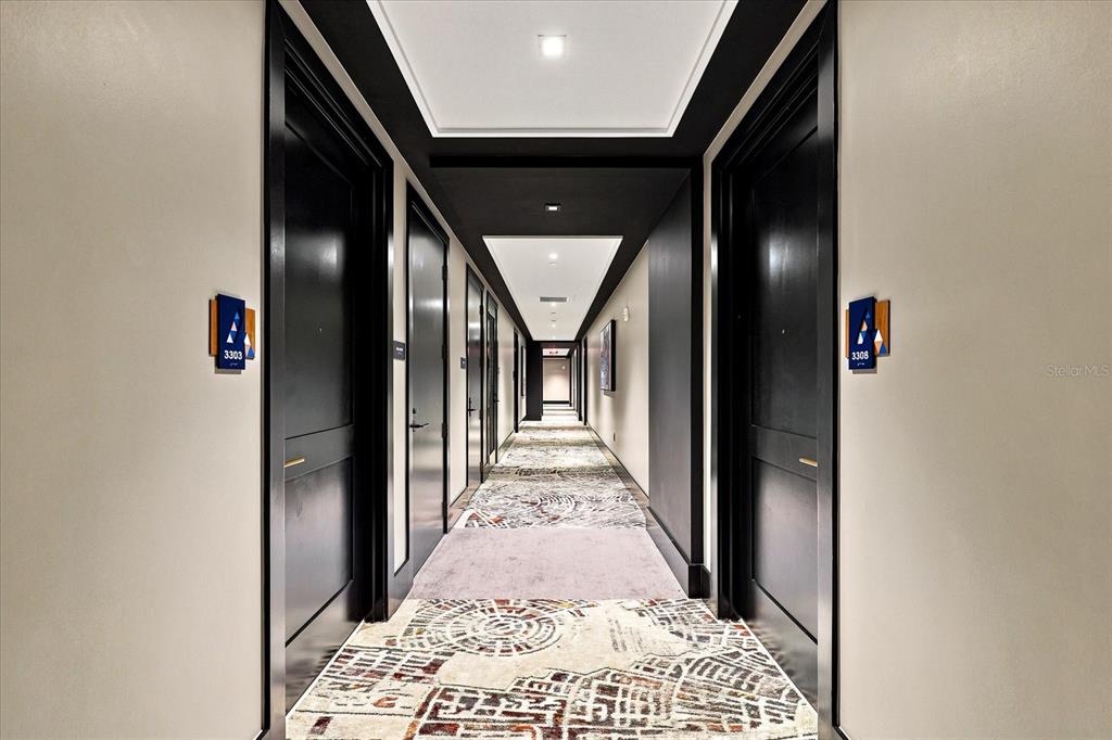 A long apartment hallway features black doors, light walls, and a patterned carpet runner — 275 1ST AVENUE S UNIT 3308, ST PETERSBURG, FL