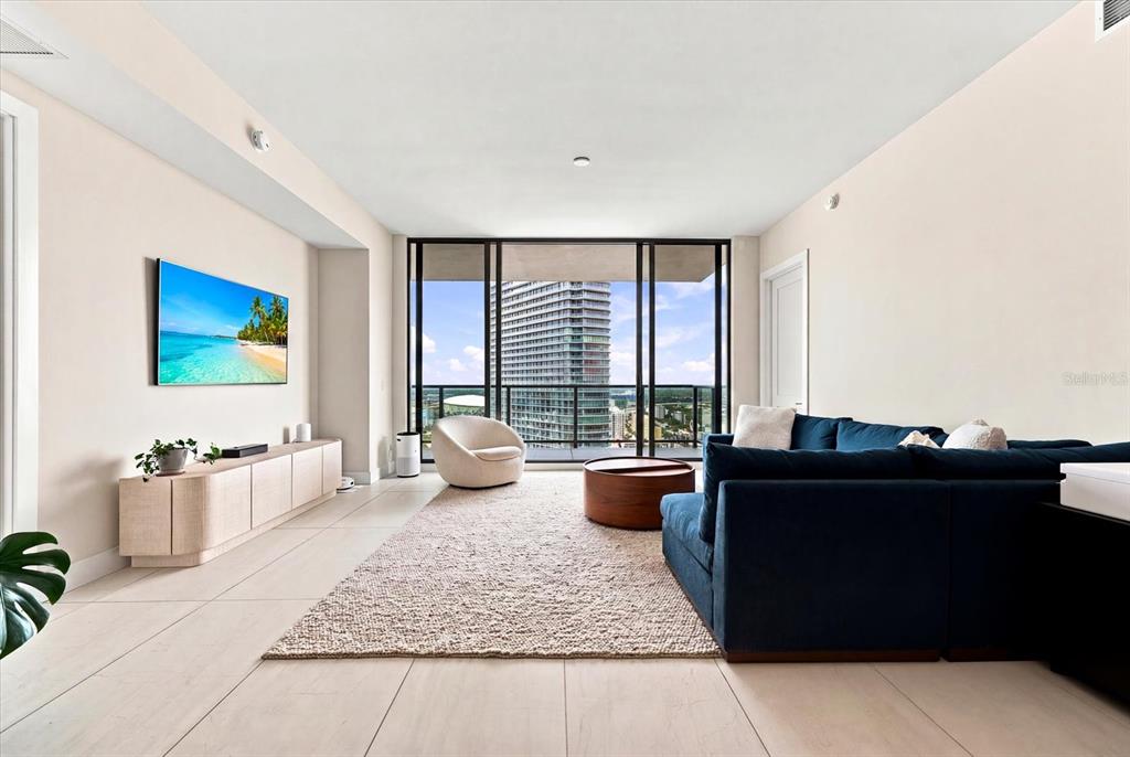 A modern living room features a blue sectional sofa, a textured rug, and floor-to-ceiling windows — 275 1ST AVENUE S UNIT 3308, ST PETERSBURG, FL