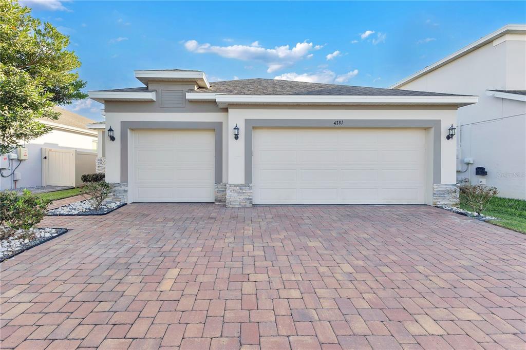 A single-story house exterior features a three-car garage, stone accents, and a paved driveway — 4781 MARCOS CIRCLE, KISSIMMEE, FL