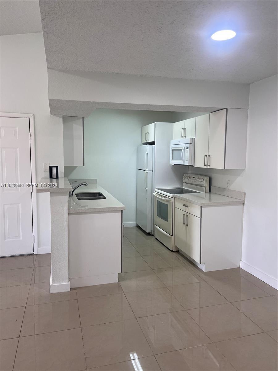 This kitchen features white cabinets, light countertops, stainless steel appliances, and beige tile flooring — 10441 SW 156th Ct # 425, Miami FL 33196, MIAMI, FL