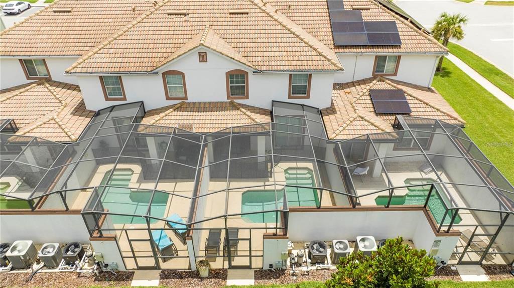 An aerial view shows three adjacent townhomes with screened-in pools and rooftop solar panels — 1568 PLUNKER DRIVE, DAVENPORT, FL