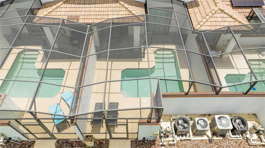 An aerial view shows three screened-in swimming pools with adjacent patio areas and exterior air conditioners — 1568 PLUNKER DRIVE, DAVENPORT, FL