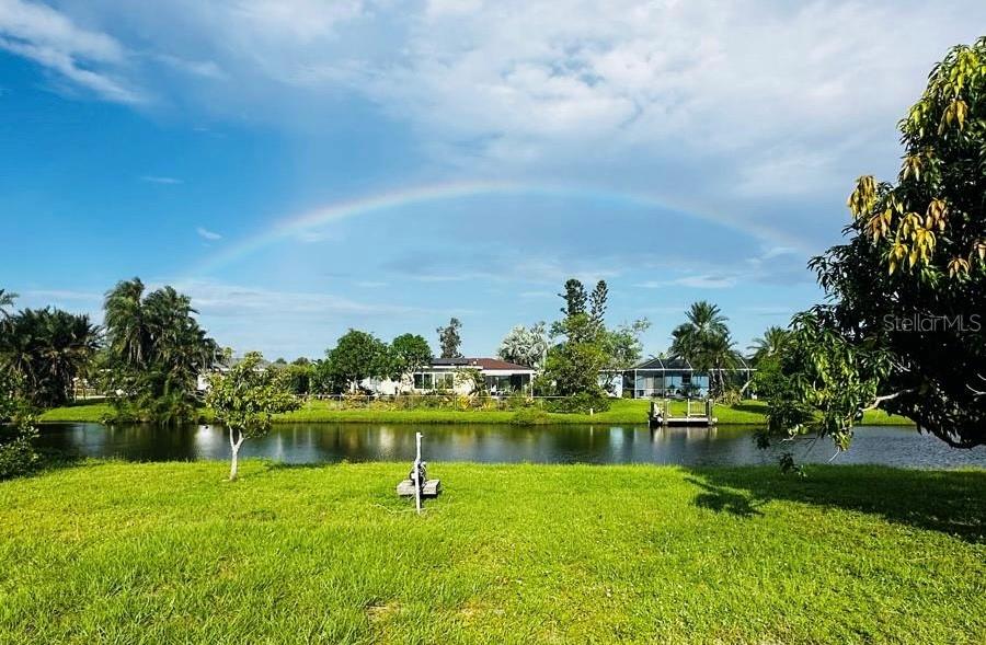A grassy backyard overlooks a canal with houses in the background under a rainbow — 130 BOUNDARY BOULEVARD UNIT A&B, ROTONDA WEST, FL