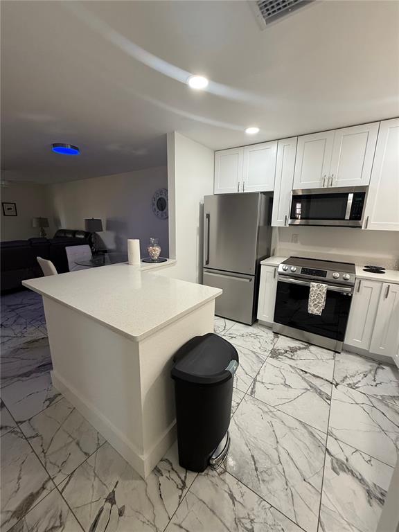 A kitchen features white cabinets, stainless steel appliances, a quartz island, and marble-patterned tile flooring — 130 BOUNDARY BOULEVARD UNIT A&B, ROTONDA WEST, FL