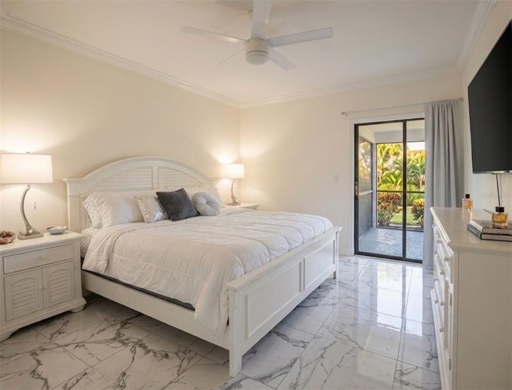A bedroom with a white bed, marble floors, and a sliding glass door to a patio — 130 BOUNDARY BOULEVARD UNIT A&B, ROTONDA WEST, FL