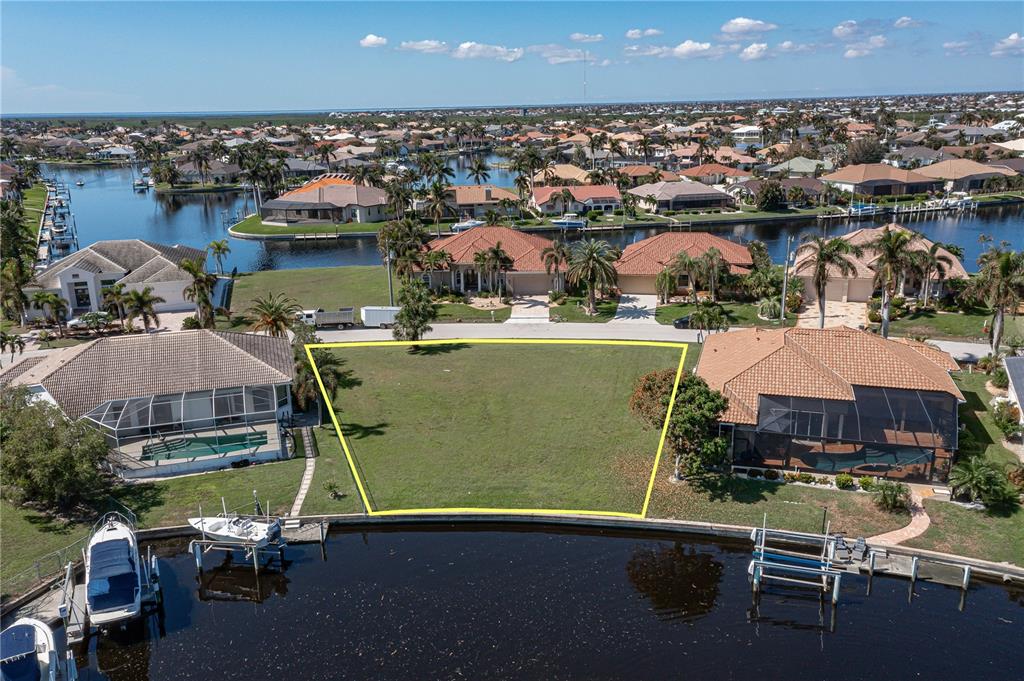 An aerial view of a vacant waterfront residential lot outlined in yellow between two houses — 3628 LICATA COURT, PUNTA GORDA, FL