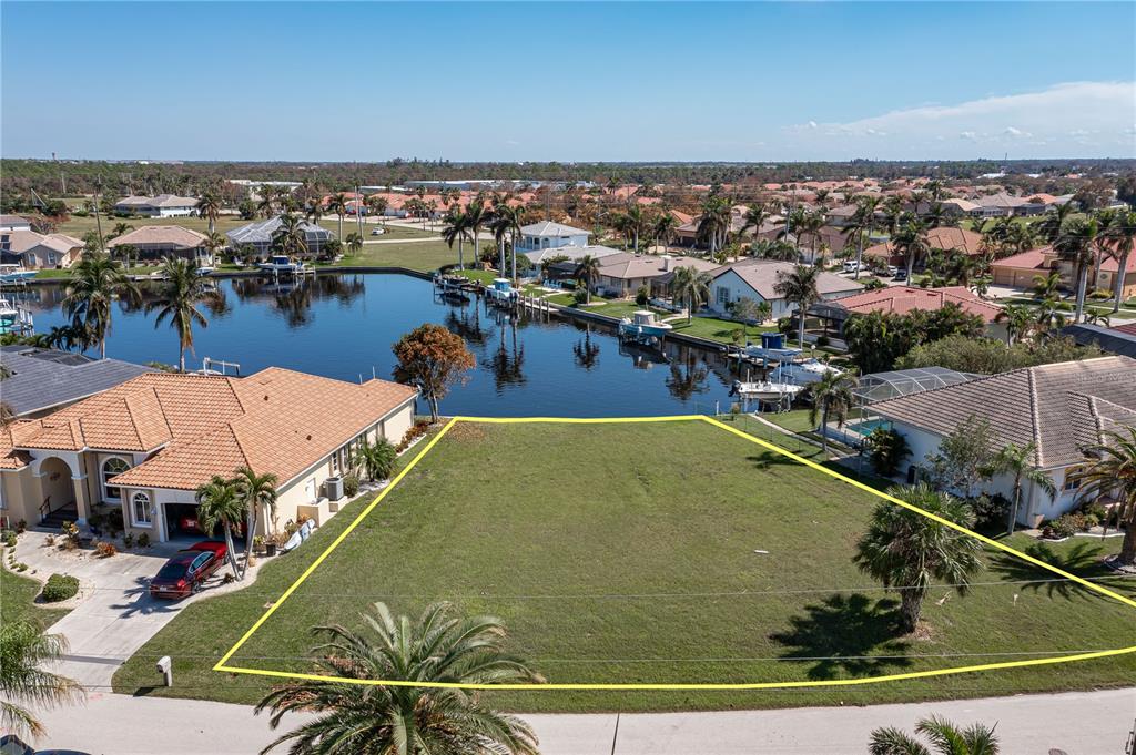 An aerial view shows a vacant waterfront lot outlined in yellow between two houses — 3628 LICATA COURT, PUNTA GORDA, FL