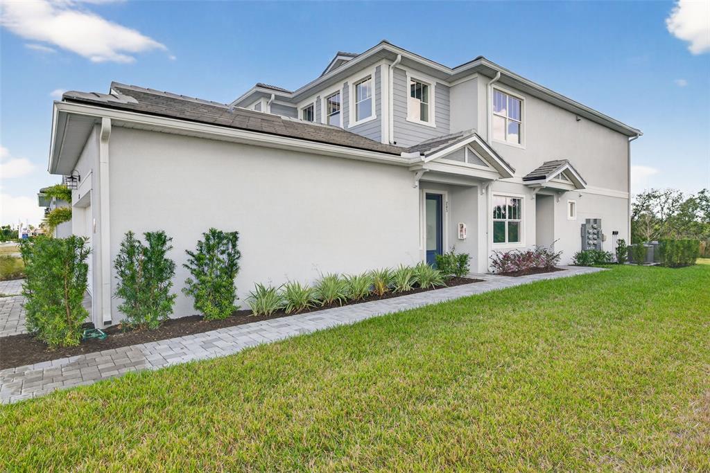 A two-story house exterior with a paved walkway, light-colored stucco walls, and green landscaping — 17375 MOONFLOWER DRIVE UNIT 203, VENICE, FL