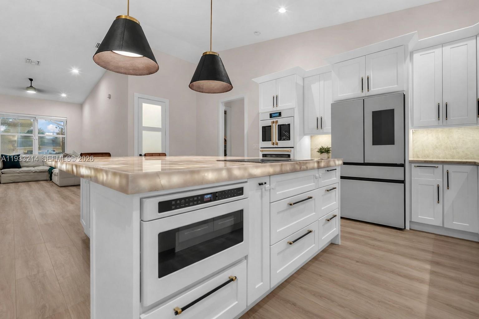 A modern kitchen features white cabinetry, a large island with a built-in microwave, and pendant lighting — 17844 N 38th Rd N, Loxahatchee FL 33470, LOXAHATCHEE, FL