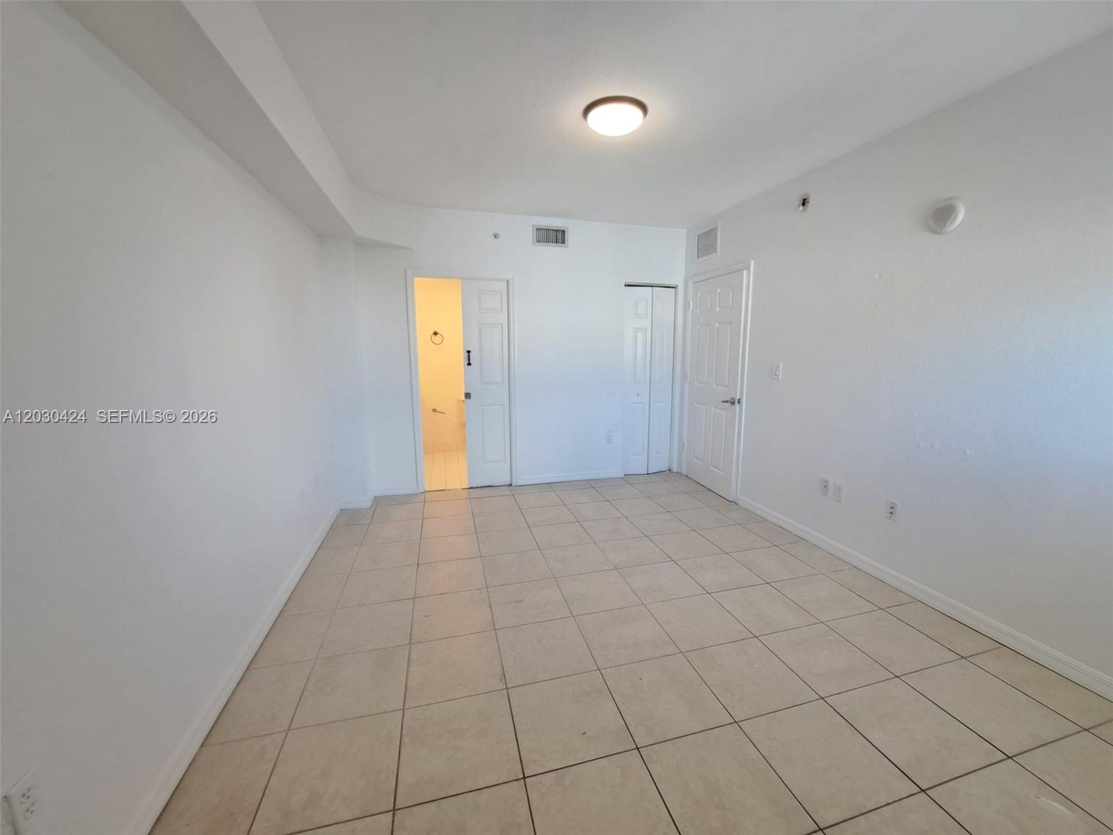 An empty room features white walls, beige tile flooring, a ceiling light, and three doors — 120 SW 8th Ave # 903, Miami FL 33130, MIAMI, FL