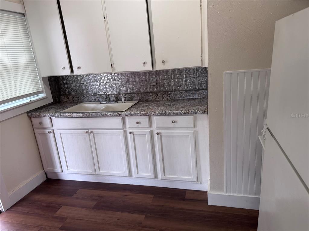 A kitchen features white cabinets, a granite countertop, a metal backsplash, and wood-look flooring — 108 E BROADWAY STREET, FORT MEADE, FL