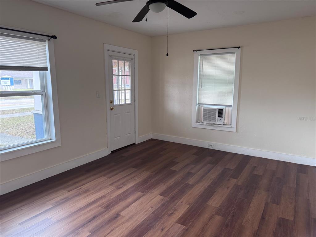 An empty room features wood-look flooring, a ceiling fan, a door, and two windows — 108 E BROADWAY STREET, FORT MEADE, FL