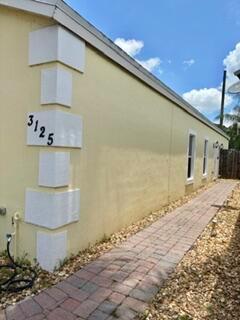 A yellow exterior wall features white corner accents, a house number, and a brick walkway — 3125 Shelby Way Way, Palm Springs FL 33461, PALM SPRINGS, FL