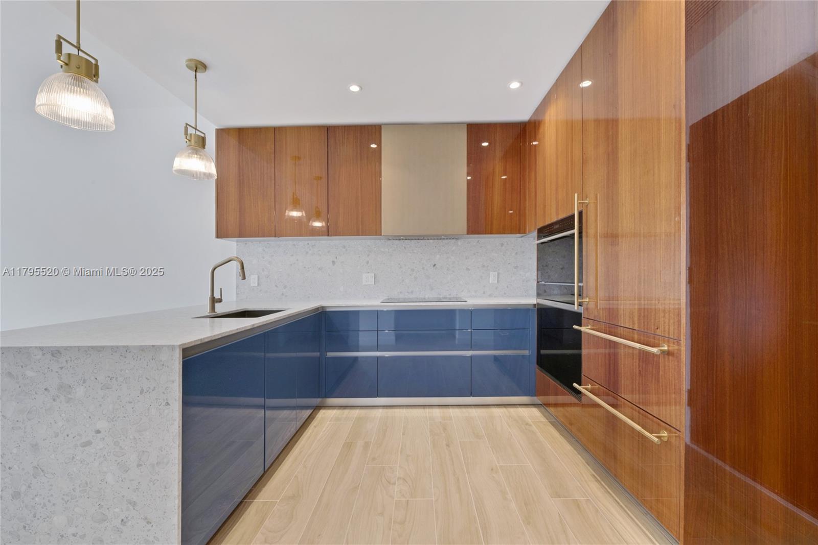A modern kitchen features blue lower cabinets, wood-toned upper cabinets, and a speckled stone countertop — 2678 Tigertail Ave # 1205, Miami FL 33133, MIAMI, FL