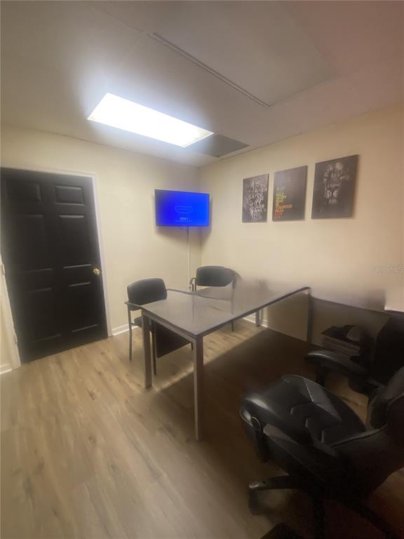 A small office room features a glass desk, black chairs, a wall-mounted television, and wood-look flooring — 7448 S US HIGHWAY 1, PORT ST LUCIE, FL