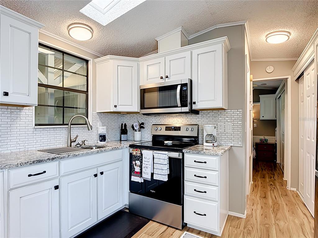 A kitchen features white cabinets, granite countertops, stainless steel appliances, and a subway tile backsplash — 9000 US HWY 192 UNIT 476, CLERMONT, FL