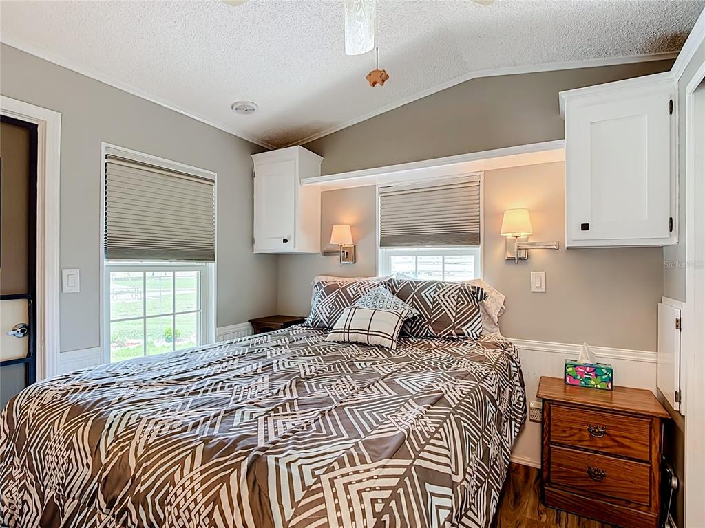A bedroom features a bed with patterned bedding, wall-mounted lamps, and white overhead cabinets — 9000 US HWY 192 UNIT 476, CLERMONT, FL