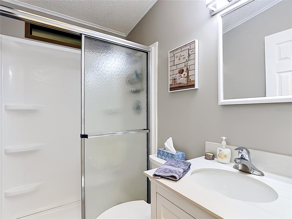 A bathroom features a white vanity, a glass-enclosed shower, and a wall-mounted mirror — 9000 US HWY 192 UNIT 476, CLERMONT, FL