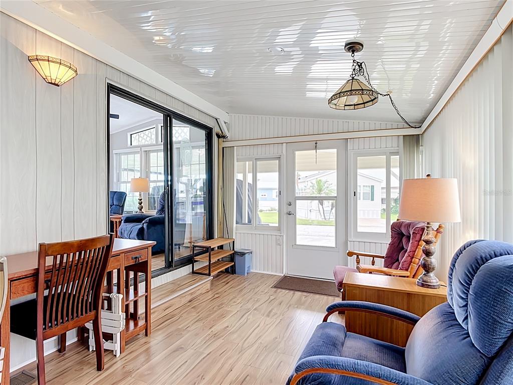 A sunroom features wood-look flooring, paneled walls, a sliding glass door, and two armchairs — 9000 US HWY 192 UNIT 476, CLERMONT, FL