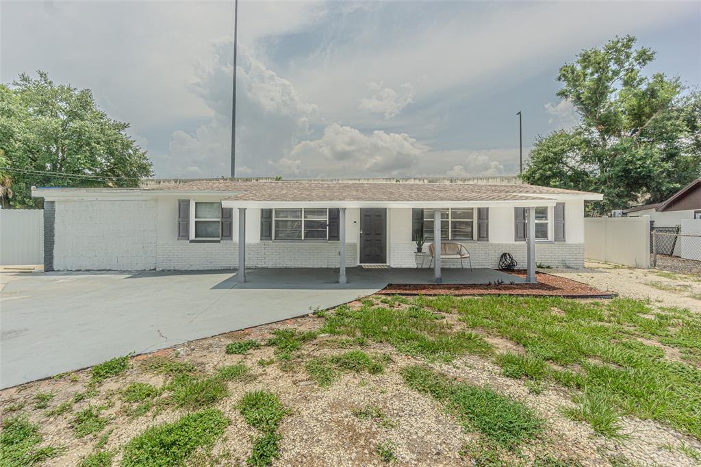 A single-story white brick house features a covered front porch and a paved driveway — 5817 E 30TH AVENUE, TAMPA, FL