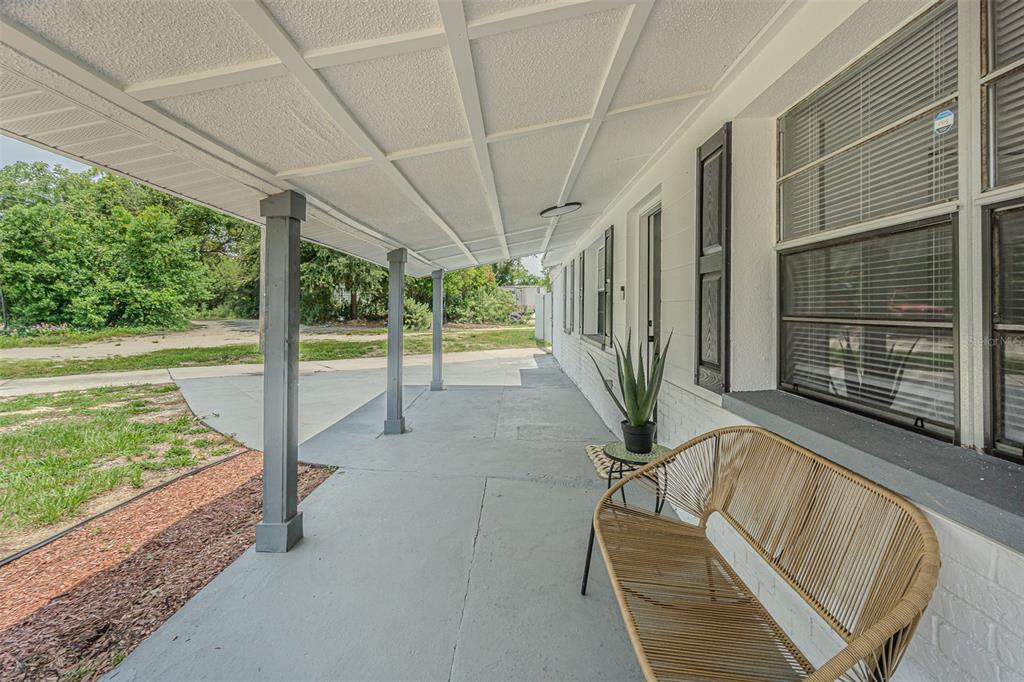 A covered concrete porch with gray support columns, a wicker bench, and a potted plant — 5817 E 30TH AVENUE, TAMPA, FL