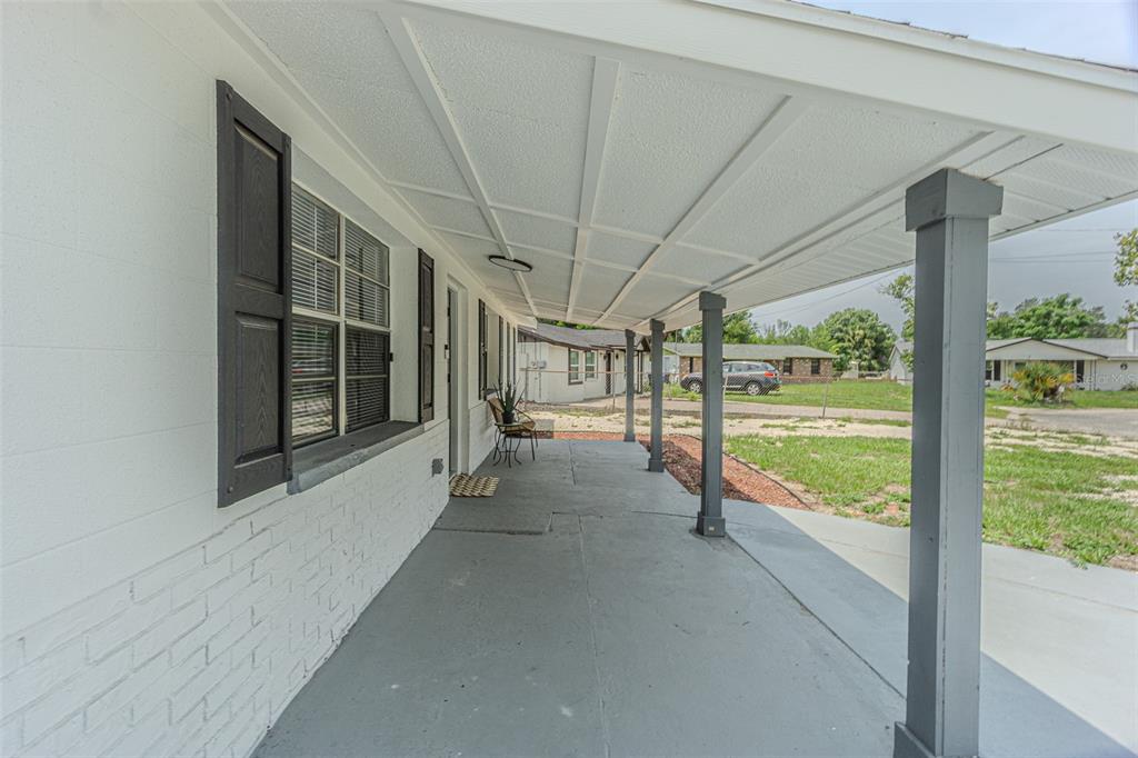 A covered concrete porch with dark support columns runs along the side of a white house — 5817 E 30TH AVENUE, TAMPA, FL