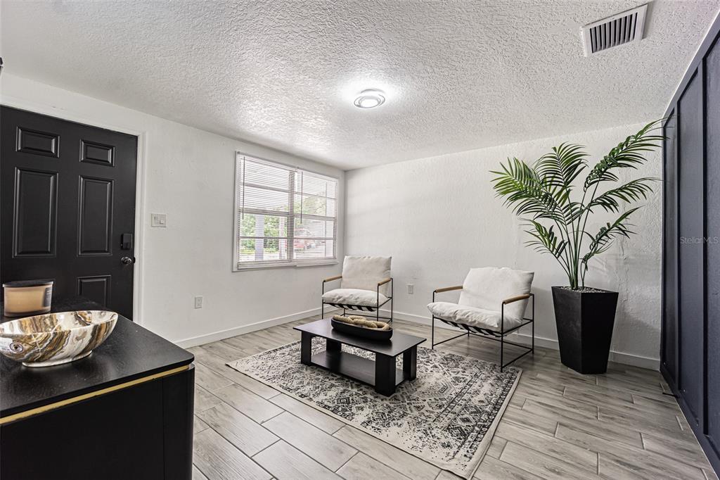 A living room features white walls, wood-look tile flooring, two armchairs, and a black door — 5817 E 30TH AVENUE, TAMPA, FL