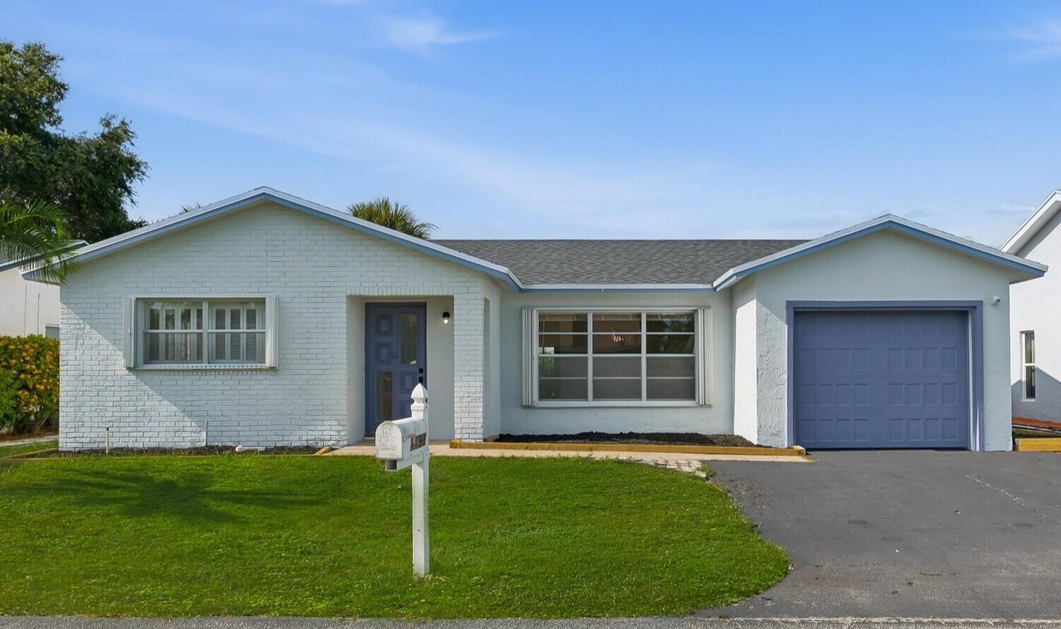 A single-story house with a white brick exterior, blue garage door, and a front lawn — 7198 E Pine Forest Cir Circle E, Lake Worth FL 33467, LAKE WORTH, FL