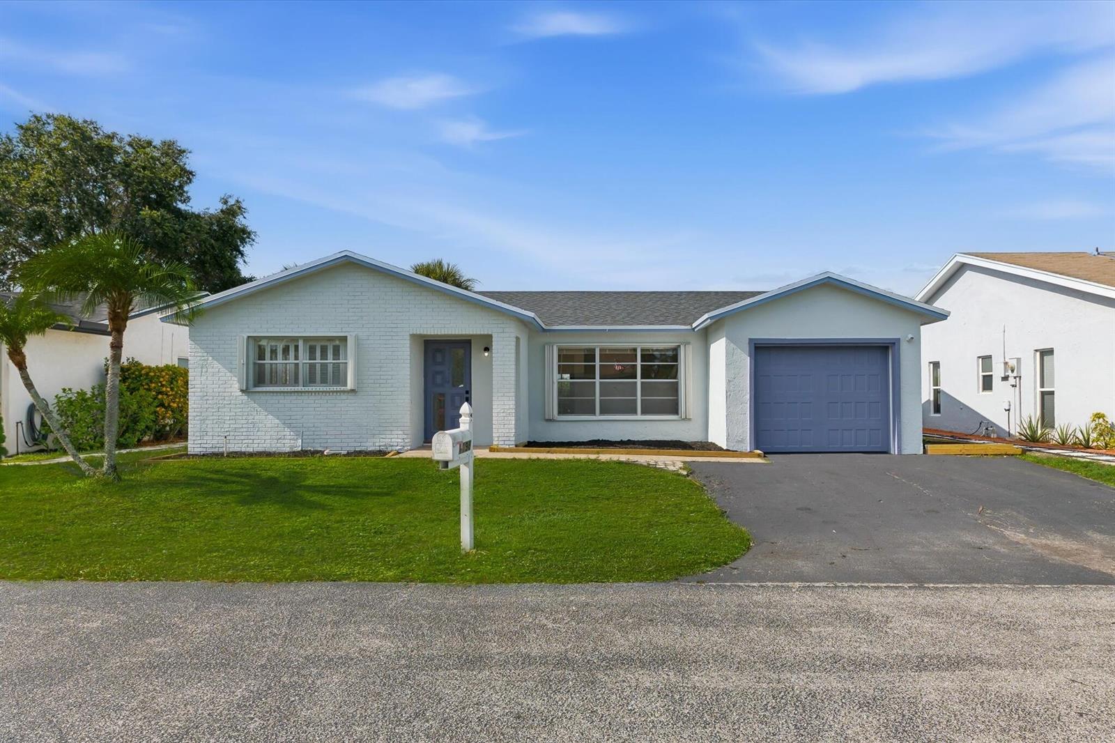 A single-story white brick house features a blue front door and a matching garage door — 7198 E Pine Forest Cir Circle E, Lake Worth FL 33467, LAKE WORTH, FL