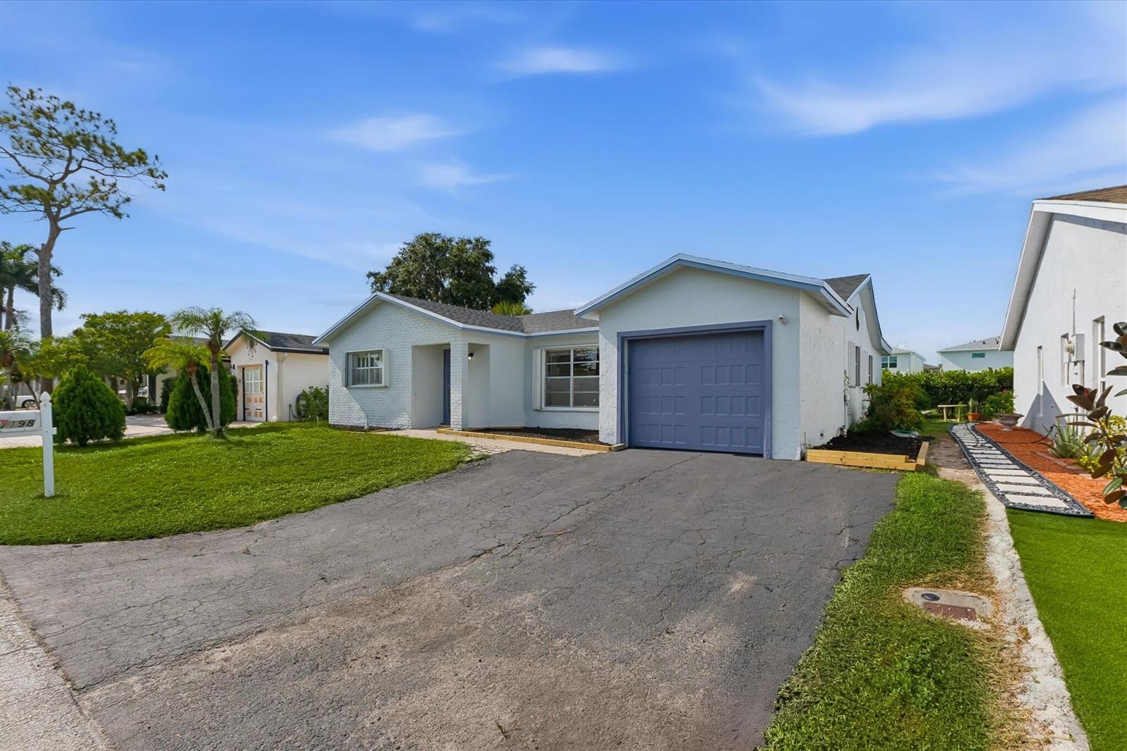 A single-story house with a white brick facade, a blue garage door, and a driveway — 7198 E Pine Forest Cir Circle E, Lake Worth FL 33467, LAKE WORTH, FL