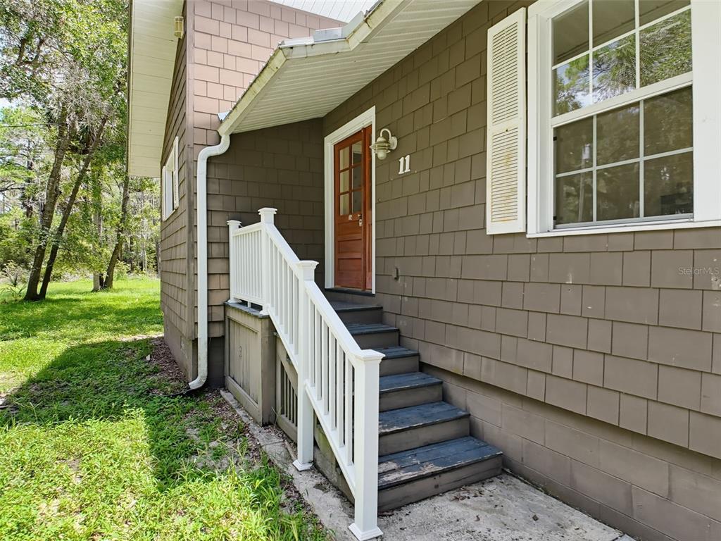 A brown house exterior features a wooden door, white railing, and stairs leading to an entrance — 11 PATRICIA ROAD, YANKEETOWN, FL