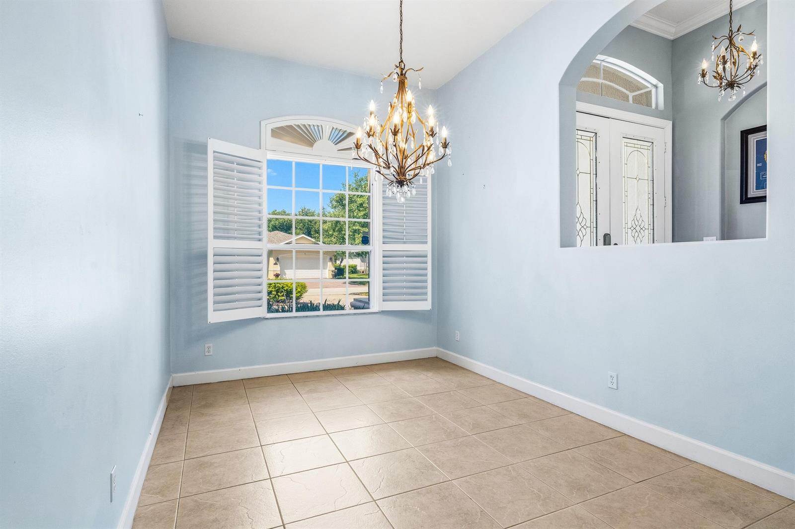 An empty dining room with light blue walls, tile flooring, a chandelier, and plantation shutters — VERO BEACH, FL