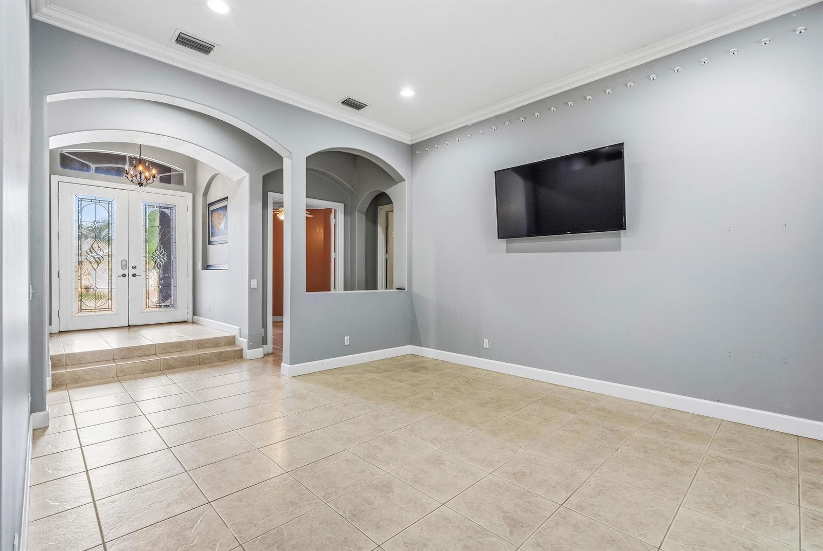 A living room with gray walls, tile flooring, an arched entryway, and a wall-mounted television — VERO BEACH, FL